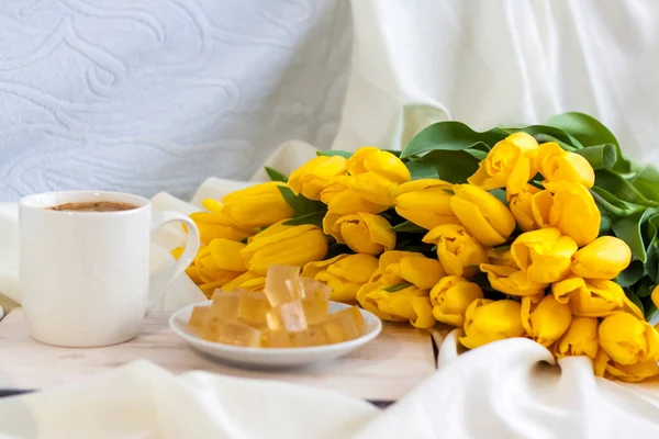 A bouquet of fresh yellow tulips and breakfast with coffee and homemade marmalade. Breakfast in bed. Spring flowers. The concept of spring and holiday, March 8, International Women\'s Day, birthday.