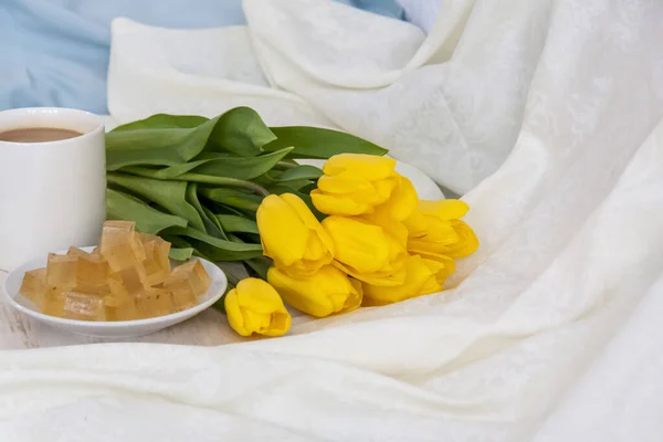 A bouquet of fresh yellow tulips and breakfast with coffee and homemade marmalade. Breakfast in bed. Spring flowers. The concept of spring and holiday, March 8, International Women\'s Day, birthday.