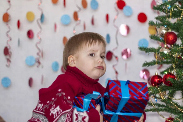 圣诞树前一个带着花环的孩子把礼物放在圣诞树下 孩子们的感情圣诞节和新年 广告横幅的概念 — 图库照片