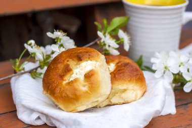 Koyu renkli, yıpranmış ahşap bir masada fırınlanmış ekmek ve bir fincan kahve. Kompozisyon beyaz çiçeklerle süslenmiş bir dal ile süslenmiş. Kiraz ağacı çiçekleri. Seçici odaklanma. Bulanık arkaplan.
