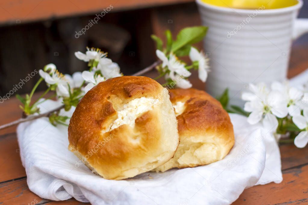 Baked open rolls and a cup of coffee on a dark, worn rustic wooden table. The composition is decorated with a twig with white flowers. Cherry tree flowers. Selective focus. Blurred background.