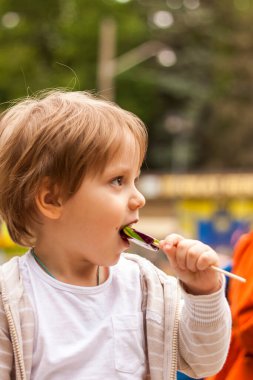Büyük yuvarlak bir lolipop tutan küçük sevimli bir çocuğun portresi. Bebek kocaman, tatlı bir lolipop yiyor. Şekerli bebek 