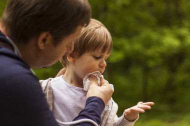 Baba küçük oğluna iyi bakıyor. Baba çocuğun yüzünü bir peçeteyle sildi. Bebek bakımı, babalık, velayet.
