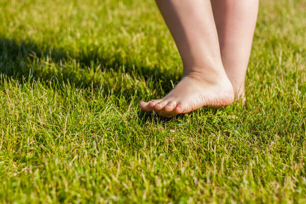 The child's bare feet on the grass. I am happy to walk and play on the lawn in warm sunny weather in the park. children's emotions, happiness