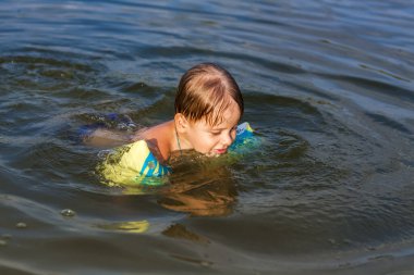 Çok sıcak bir yaz gününde mutlu bir çocuk nehirde yüzüyor. Su depolarında yüzmek. Mutlu bir aile yazın eğlenir ve suya su sıçratır. Aile tatilde.