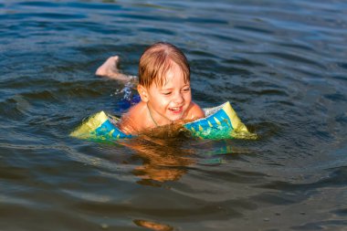 Çok sıcak bir yaz gününde mutlu bir çocuk nehirde yüzüyor. Su depolarında yüzmek. Mutlu bir aile yazın eğlenir ve suya su sıçratır. Aile tatilde.