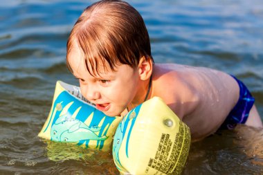 Çok sıcak bir yaz gününde mutlu bir çocuk nehirde yüzüyor. Su depolarında yüzmek. Mutlu bir aile yazın eğlenir ve suya su sıçratır. Aile tatilde.