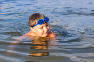 Çok sıcak bir yaz gününde mutlu bir çocuk nehirde yüzüyor. Su depolarında yüzmek. Mutlu bir aile yazın eğlenir ve suya su sıçratır. Aile tatilde.