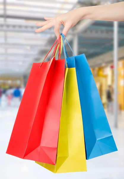 Ženská ruka drží nákupní tašky s pozadím shopping mall — Stock fotografie