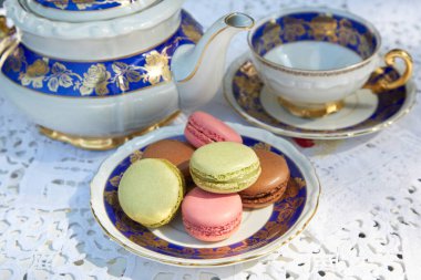 Seramik çaydanlık ve fincanlı makarna bisküvileri, beyaz işlemeli masa örtüsü.