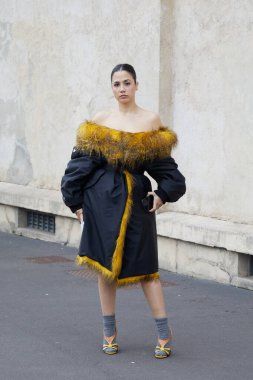 MILAN, ITALY - JANUARY 18, 2026: Woman with dark dress with yellow fur border and high heel shoes with socks before Prada fashion show, Milan Fashion Week street style