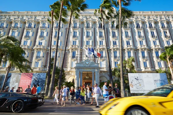 People walking and luxury cars passing under palm trees in Cannes