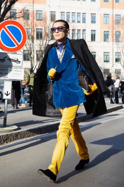 Man with blue velvet jacket and yellow trousers poses for photographers before Emporio Armani fashion show