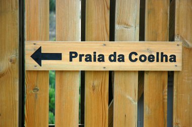 Tahta tabela Praia da Coelha ya da Rabbit Sahili 'ne doğru giden yolu gösteren tahta bir çite yerleştirilmiş. Albufeira, Algarve, Portekiz belediyesinde kaya oluşumlarıyla çevrili küçük bir plaj.