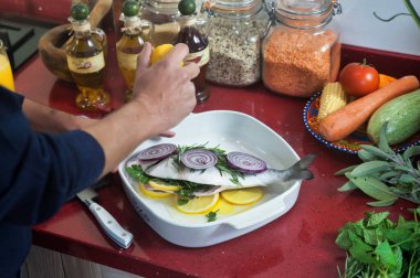 Beyaz tenli bir adam, beyaz bir fırında bütün bir balığı hazırlıyor. Limon, soğan halkaları ve taze otlarla süslüyor. Üstüne de taze limon suyu serpiştiriyor.