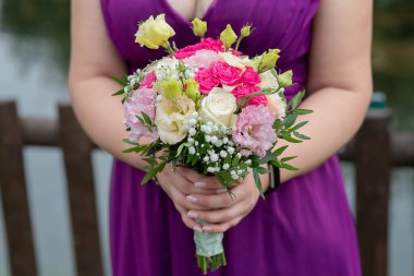 Kafkasyalı nedime güzel mor bir elbise giyiyor ve elinde yuvarlak bir buket tutuyor. Gelinin düğün partisi için mükemmel bir kıyafet. Ellerinde zarif çiçek aranjmanı var.