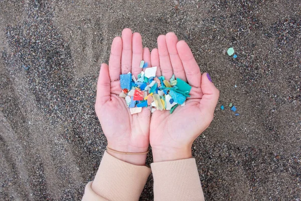 Woman holding a hand full of colorful plastic fragments, litter collected from the beach, polluting the ocean and putting wildlife in danger, environmental effort and duty to recycle and reduce waste