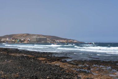 El Medano, Tenerife, Kanarya Adaları, İspanya - 23 Temmuz 2021: Montana Pelada 'ya doğru yaz manzarası sörf ve rüzgar sörfü yapan sörfçülerle birlikte