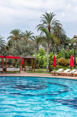 Hotel Botanico And The Oriental Spa Garden - September 19, 2024: turquoise swimming pool surrounded by wooden loungers with white cushions and several red parasols, elegant vibe and resort atmosphere