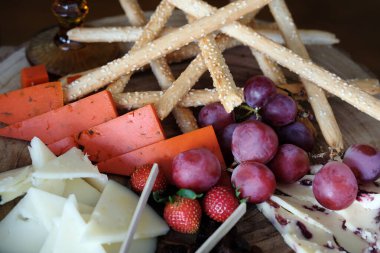 Çeşitli süslü peynirlerden oluşan yuvarlak ahşap bir tahtanın üzerinde Rustik peynir ve tapas çeşitleri, yarı tedavi edilmiş beyaz, yaban mermerinden yapılmış ve baharatlı, üzüm, çilek ve ekmek çubuklarıyla eşleştirilmiş.