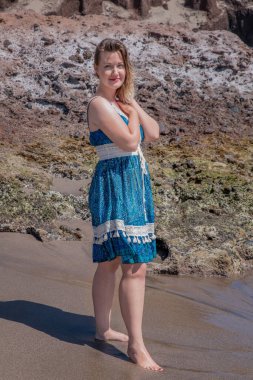 Kolsuz mavi desenli bir yaz elbisesi giymiş güzel bir kadın ellerini nazikçe göğsüne kenetleyerek La Tejita, Tenerife, İspanya 'nın Kanarya Adaları sahilinde çıplak ayakla duruyordu. 