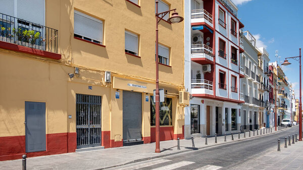 Triana, Seville, Andalusia, Spain - June 26, 2019: views of a quiet street with traditional residential buildings, colorful facades in vibrant Mediterranean colors and balconies with window shutters