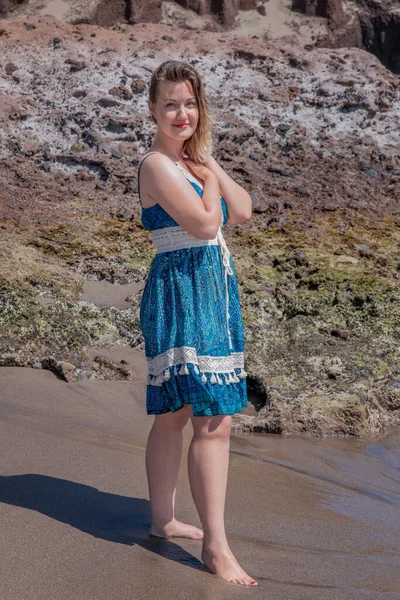 Kolsuz mavi desenli bir yaz elbisesi giymiş güzel bir kadın ellerini nazikçe göğsüne kenetleyerek La Tejita, Tenerife, İspanya 'nın Kanarya Adaları sahilinde çıplak ayakla duruyordu. 