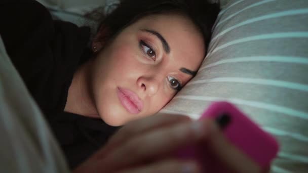 ベッドに横になってスマホを見ている若い女性 — ストック動画
