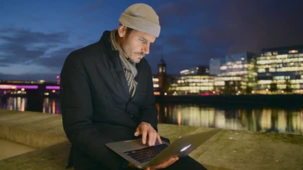 夜にテムズ川のノートパソコンを使ってコートを着た男 — ストック動画
