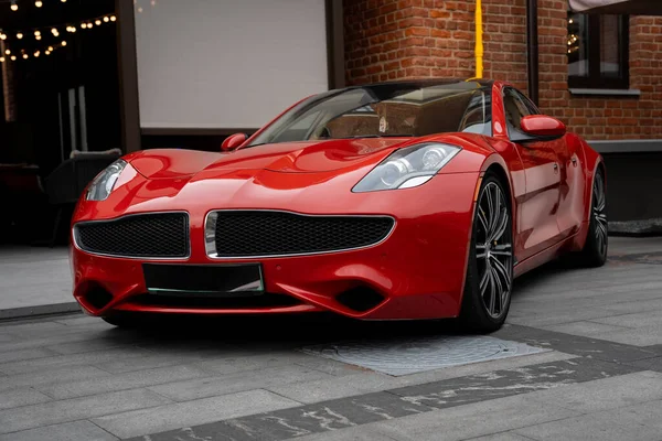 Red sports car parked elegantly on a city street near a brick building. The vehicles modern design with sharp lines and a shiny exterior enhances the urban setting