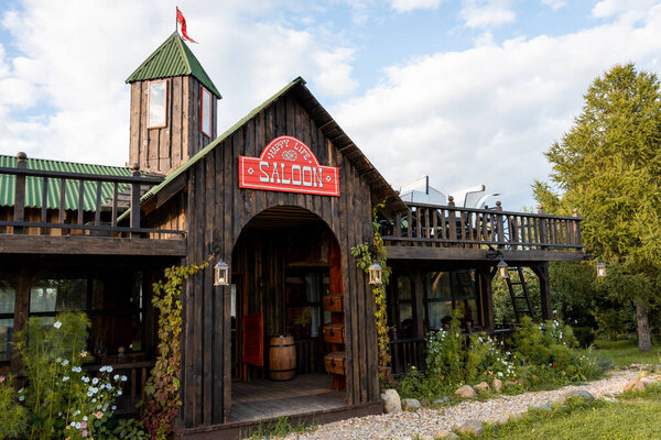 Wooden saloon building with rustic architecture, featuring a prominent Saloon sign. Surrounded by lush greenery and vibrant flowers, the setting offers a nostalgic western vibe