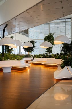 Benzersiz kıvrımlı bankları ve büyük sallanan ışıkları olan modern bir avlu. Yeşilliklerle çevrili tasarım, ahşap zeminli ve yüksek tavanlı çağdaş bir açık alana sahip, davetkar bir atmosfer yaratıyor.