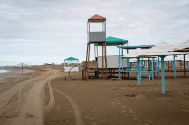 Boş cankurtaran kuleleri ve terk edilmiş sahil yapılarının olduğu terk edilmiş bir sahil manzarası. Sahne, sezon dışı sahnenin sessiz ve izole atmosferini yakalıyor.