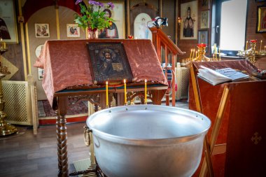 Kilisenin içinde dini simgeler ve süslü sunaklarla çevrili vaftiz fontu olan bir görüntü. Atmosfer dingin, inancı ve geleneği ön plana çıkarıyor.