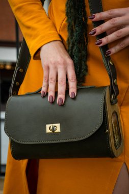 Bir kadının elleri şık bir el çantası ve şık bir kıyafet sergiliyor. Görüntü modern stili, zarif tırnakları ve modaya uygun bir sofistike anlayışı vurguluyor.