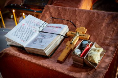 Üzerinde gözlük olan, ahşap bir haç ve mumlarla çevrili dini kitabı aç. Kurulumda küçük kaplar ve zengin desenli bir kumaş üzerinde bir parça ekmek yer alıyor.