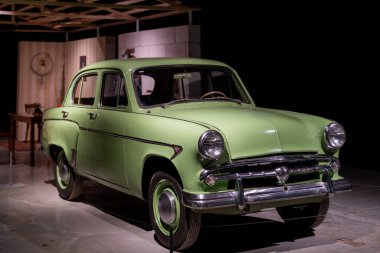 Klasik tasarım ve tarihsel özellikleri vurgulanarak kapalı bir sergide sergilenen klasik açık yeşil araba. Ayar, periyot dekoru ve çevresindeki elementleri içeriyor