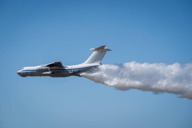 Büyük hava araçları büyük yangınlarla savaşmak için geniş bir su akışını serbest bırakır. Bu da havadan ateş etme kabiliyetini gösterir. Görüntü, uçağın açık mavi gökyüzüne karşı çarpışmasını yakalar.