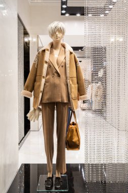 Modern bir giyim mağazasına yerleştirilmiş, yün ceketli ve aksesuarlı şık kahverengi takım elbiseli manken. Dekor çağdaş moda ve perakende zarafeti vurguluyor