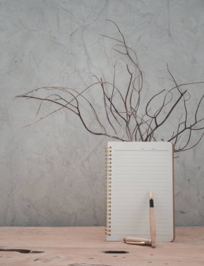 Boş defter ve ahşap kalemle tavan arası beton arka planı olan ahşap masa, ürünler için alan