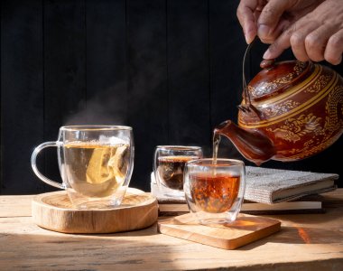 Geleneksel kil çaydanlık ve tarçınlı çay fincanı koyu ahşap masa arkasına çubuk şekeri dökülüyor.