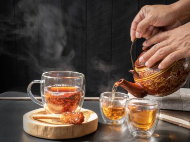 Geleneksel kil çaydanlık ve tarçınlı çay fincanı koyu ahşap masa arkasına çubuk şekeri dökülüyor.