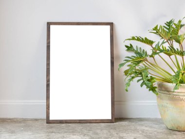 Poster ahşap çerçevesini ve Philodendron xanadu botanik evi bitkisini modern oturma odasındaki seramik kapta seramik güzel bir şekilde yerleştirin. Çatı katı zemin ve beyaz duvarlı.