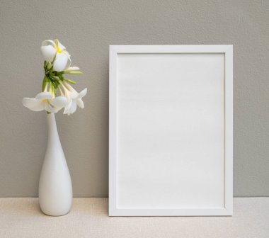 Beyaz poster çerçevesi ve güzel Plumeria ya da Frangipani tropikal çiçeğini bej masa ve çimento duvar arka planında modern beyaz vazoda taklit et. 