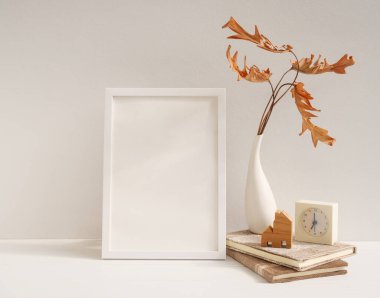 Beyaz ahşap poster çerçevesini, Philodendron kurumuş yaprağı vazo, saat, kitaplar, bej masa ve duvarda ev modeli, modern stil ev dekorasyonu.