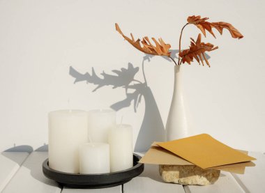 Taş podyum düğün davetiyesi zarfında tebrik kartı modeli Philodendron kurutulmuş yaprak vazosu, beyaz ahşap masa odasındaki mumlar uzun gölgeli arka plan.