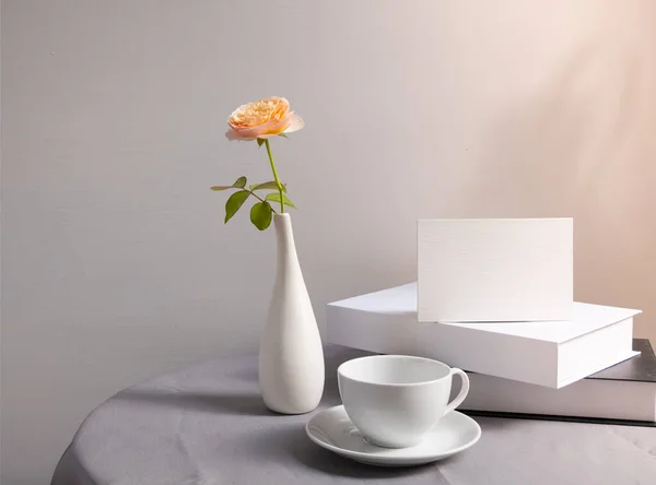 将白色的邀请卡 咖啡杯和美丽的橙红色玫瑰插在镶嵌在亚麻布桌布上的现代花瓶里 用白色的木料做衬托 柔和的问候卡片静止不动 — 图库照片