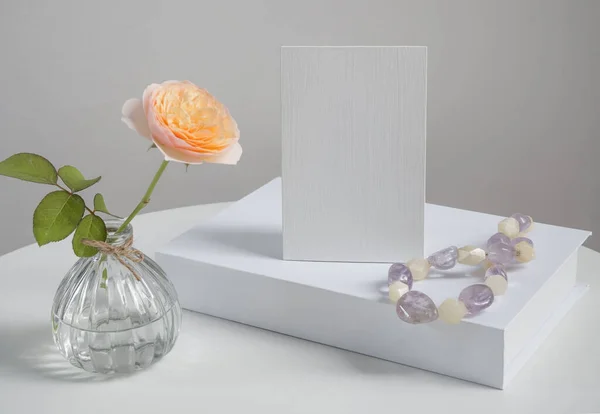 白いテーブルの背景にアメジストとクォーツネックレスとモックアップ招待カードとホワイトブックの装飾とガラス花瓶の美しいバラの花 — ストック写真