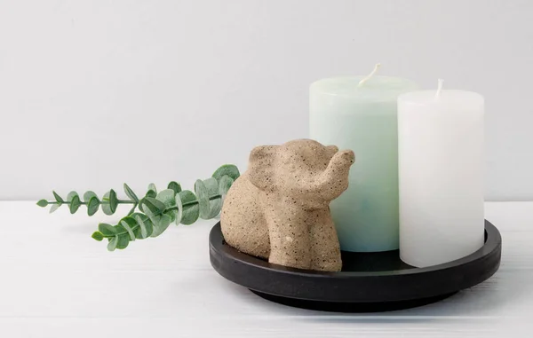 Candles,elephant and Eucalyptus leave on  black wooden tray in whiye room interior,spa composition products