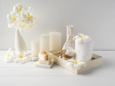 Spa kompozisyonu masaj Hearbel Ball, vazoda plumeria çiçeği, hindistan cevizi kahve sabunu, beyaz havlular ve beyaz ahşap masa zemininde mum, yumuşak beyaz ton natürmort hayat.